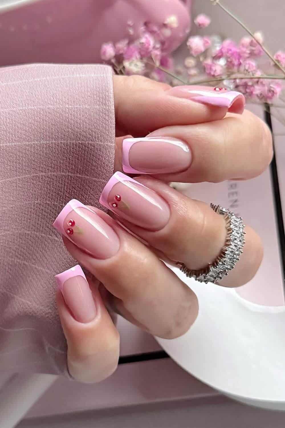 Design your pink nails with these delicate, calm pink French tips. The two nails adorned with tiny pink gemstones add a subtle sparkle that looks practical and chic. The pink nail design evokes the gentle beauty of summer blossoms while maintaining elegance.